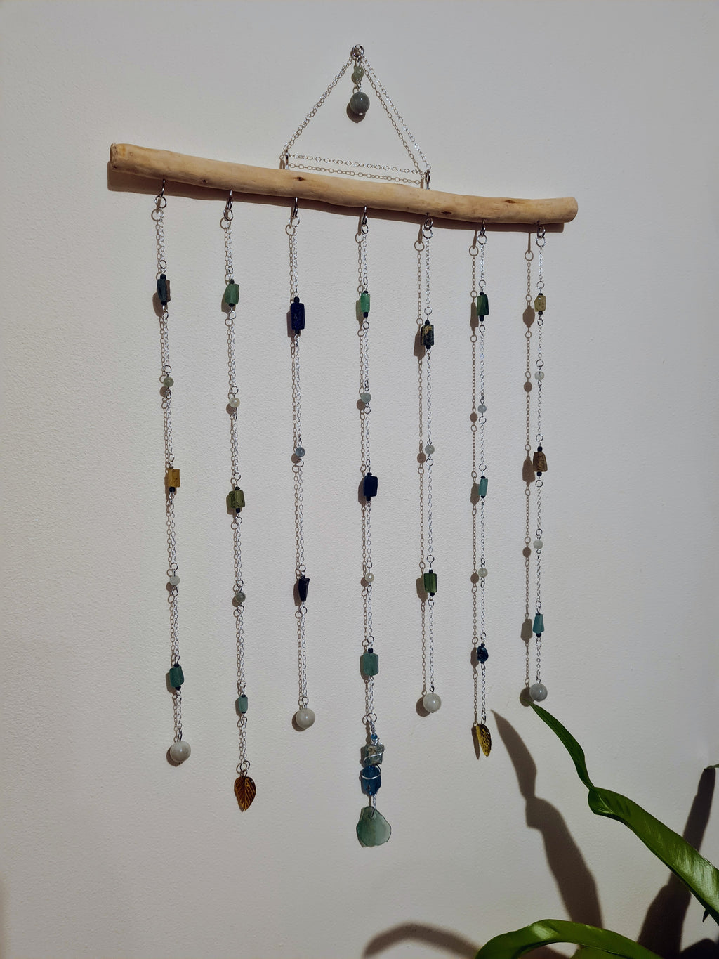Decorative wall hanging with  Roman glass and Aquamarine beads hanging from a branch against a plain background