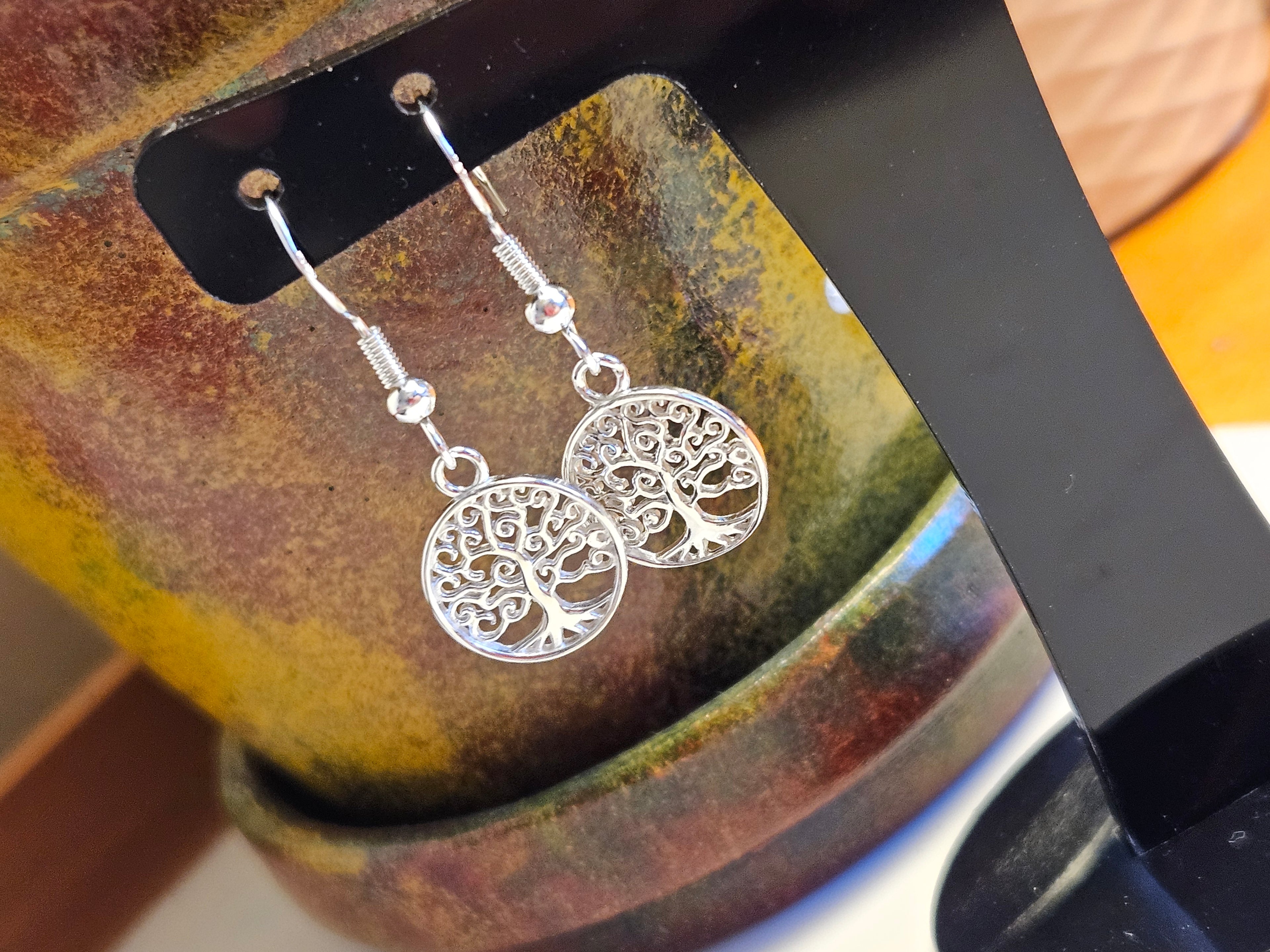 Silver tree-of-life earrings on a black stand with a colorful background
