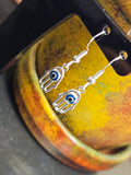 Silver hamsa hand earrings with blue eyes on a textured surface