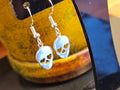 Silver sugar skull earrings on a yellow background