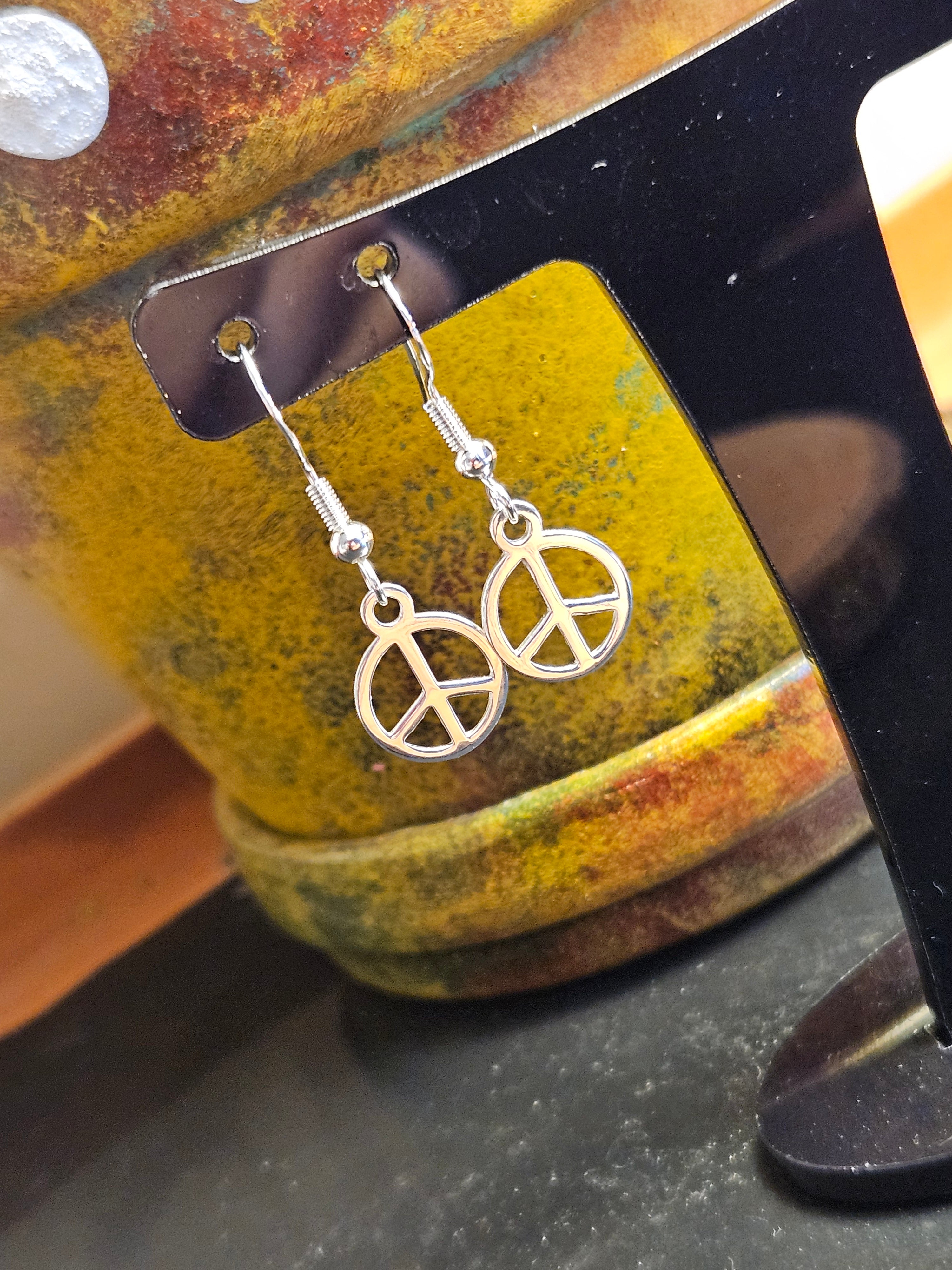 Silver peace symbol earrings hanging from a black stand