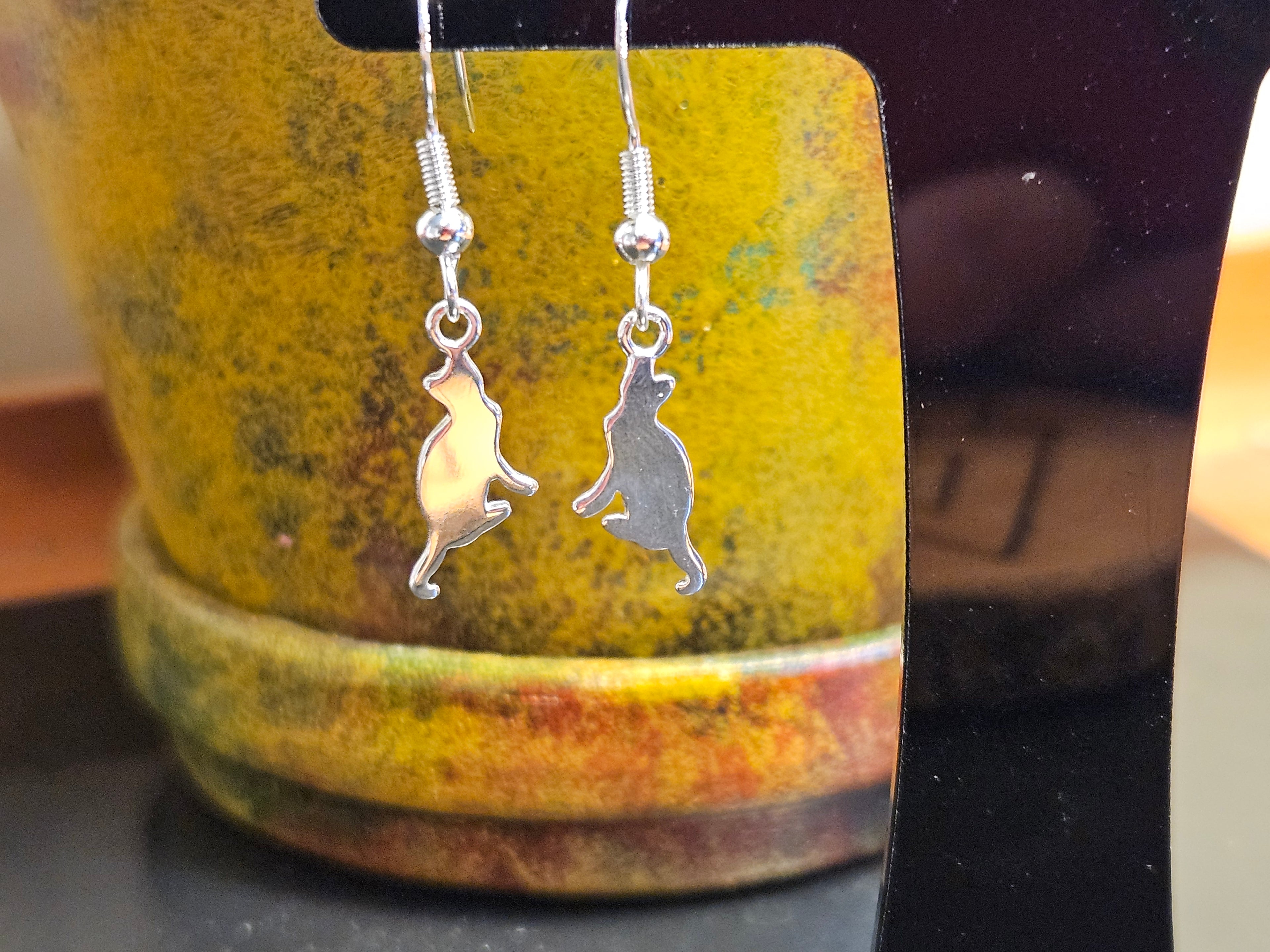 Silver cat shaped earrings hanging from a black stand
