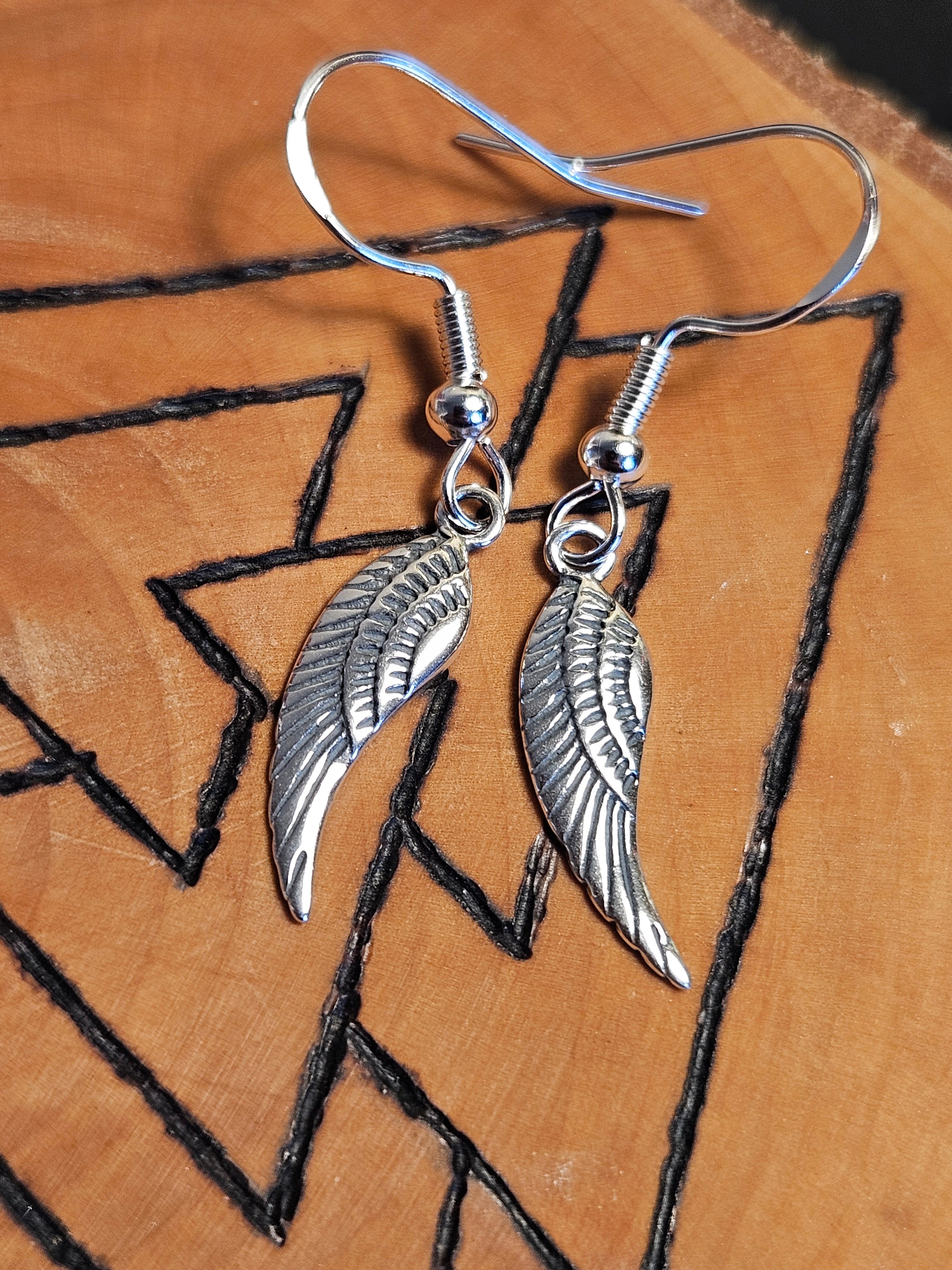 Silver wing-shaped earrings on a wooden surface with black line art.