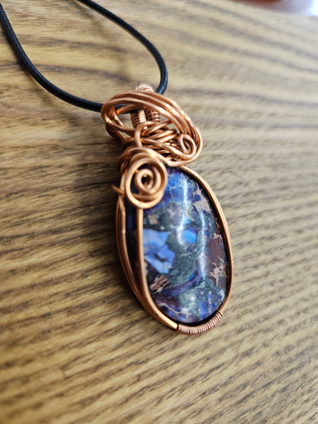 Copper-wrapped pendant with a blue and purple Sediment Jasper stone on a wooden surface