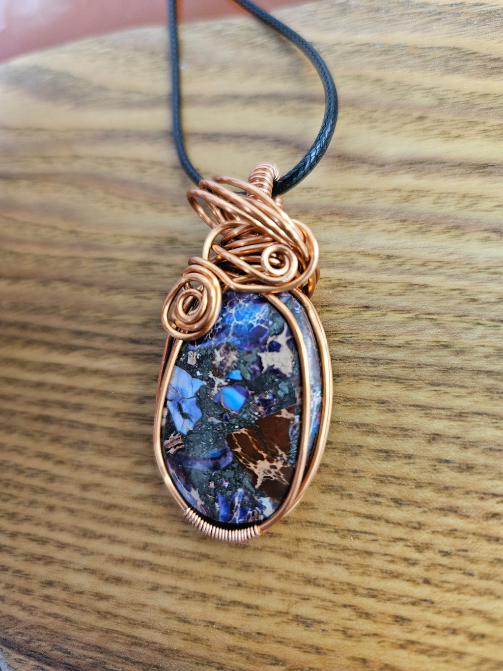 Jewelry pendant with blue stone and copper wirework on a wooden surface
