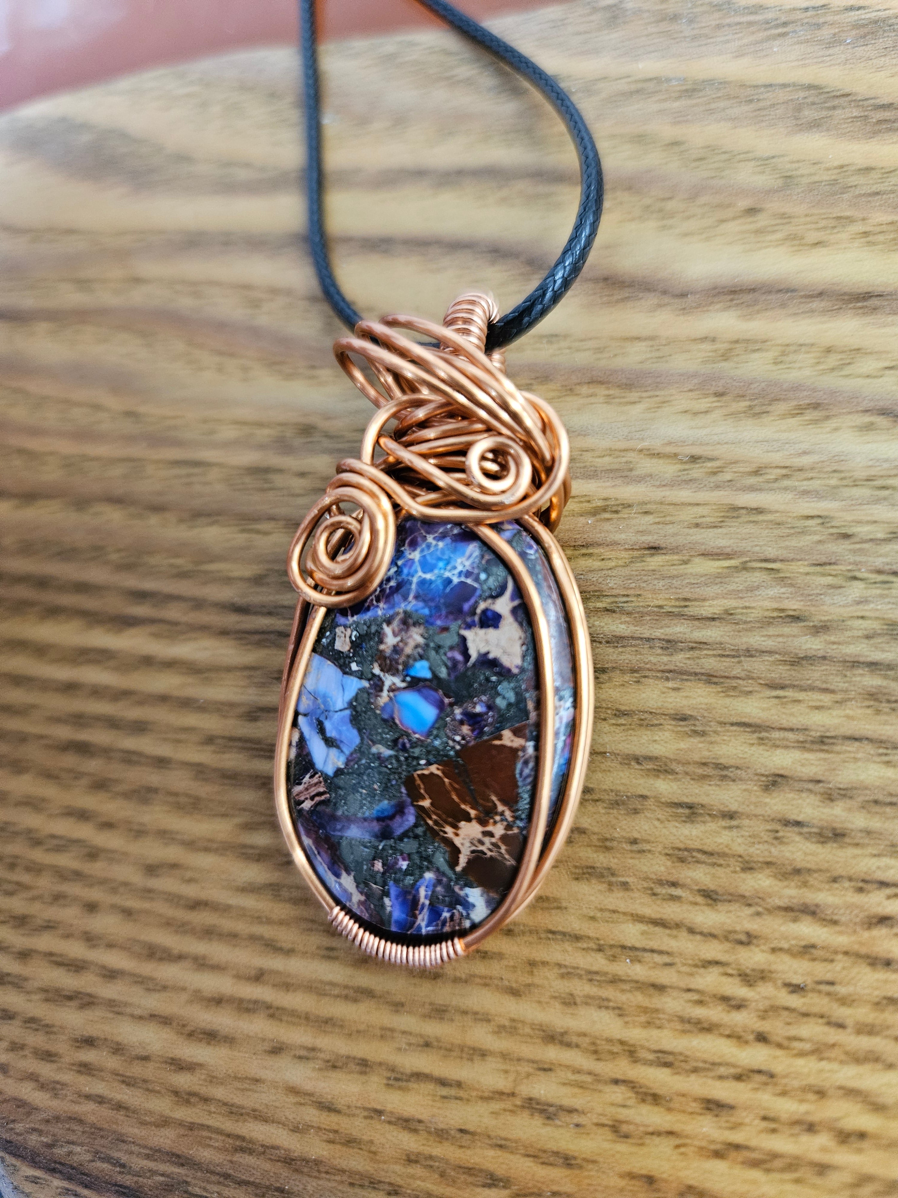 Jewelry pendant with blue stone and copper wirework on a wooden surface