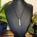 Necklace with a crystal pendant on a black mannequin bust, with plants in the background.