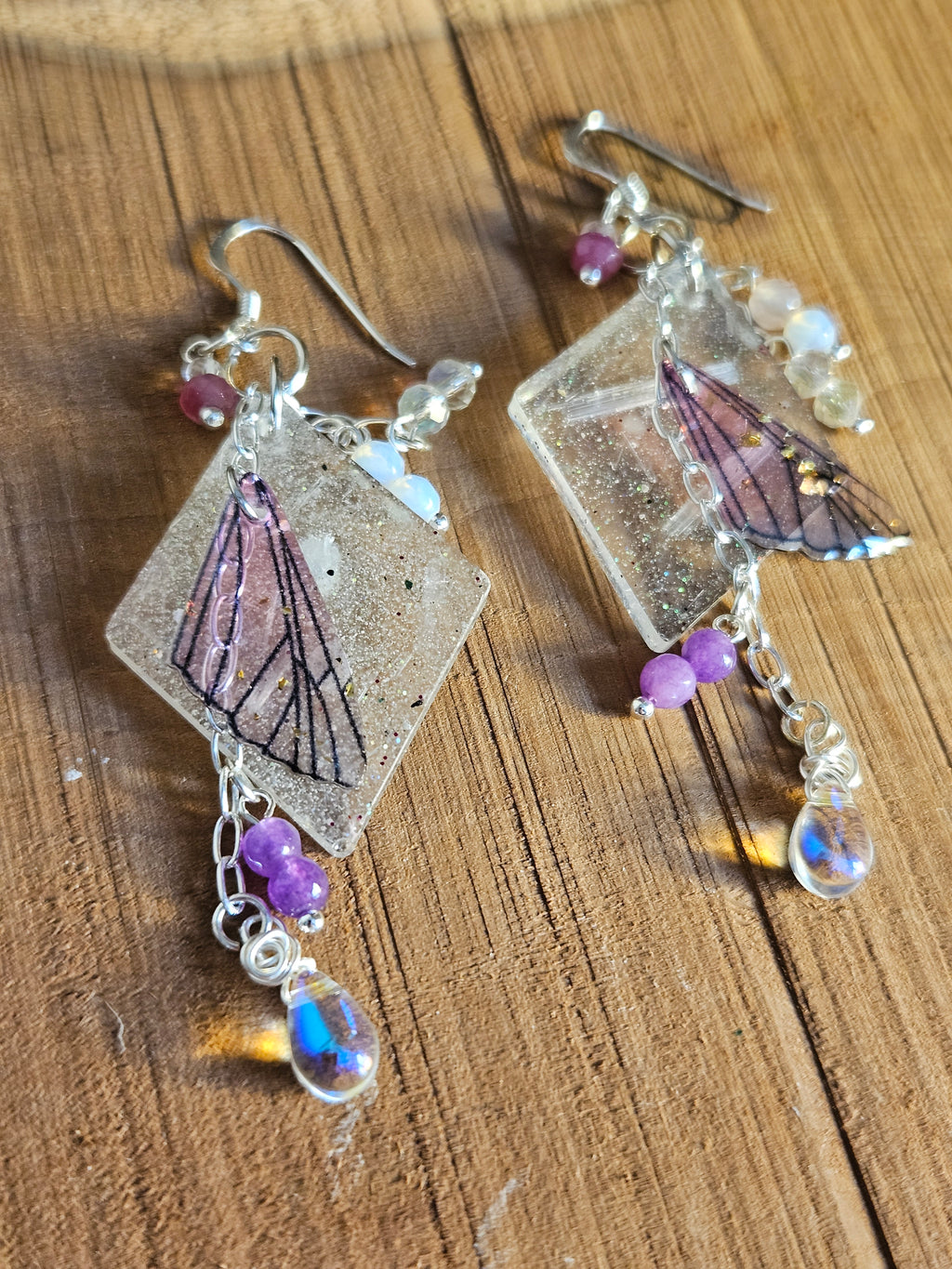 Butterfly-themed earrings with gemstones on a wooden surface