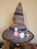 Crocheted witch hat with floral decorations on a beige surface