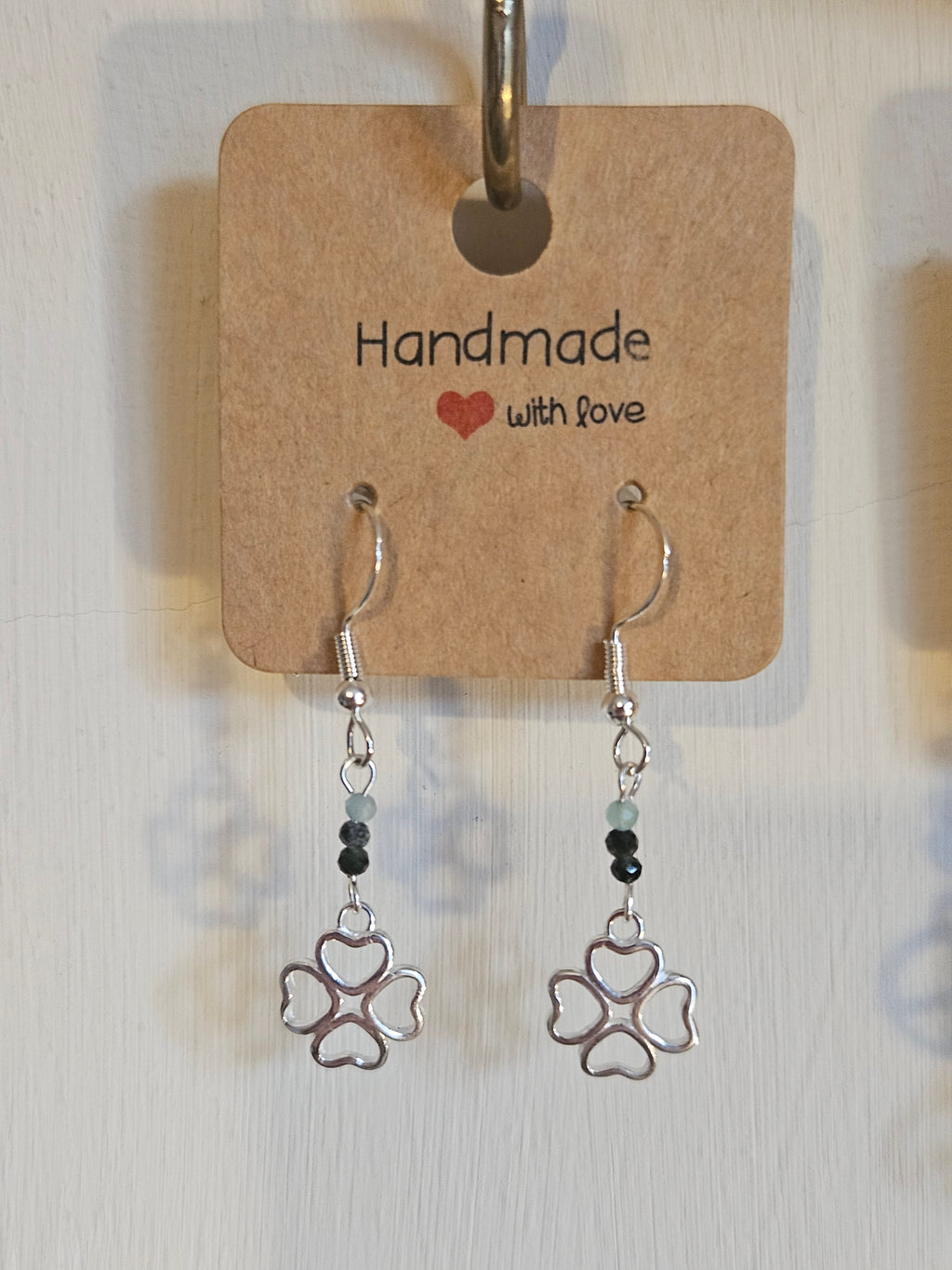 Pair of silver earrings with 4 leaf clover design on a 'Handmade with Love' card.
