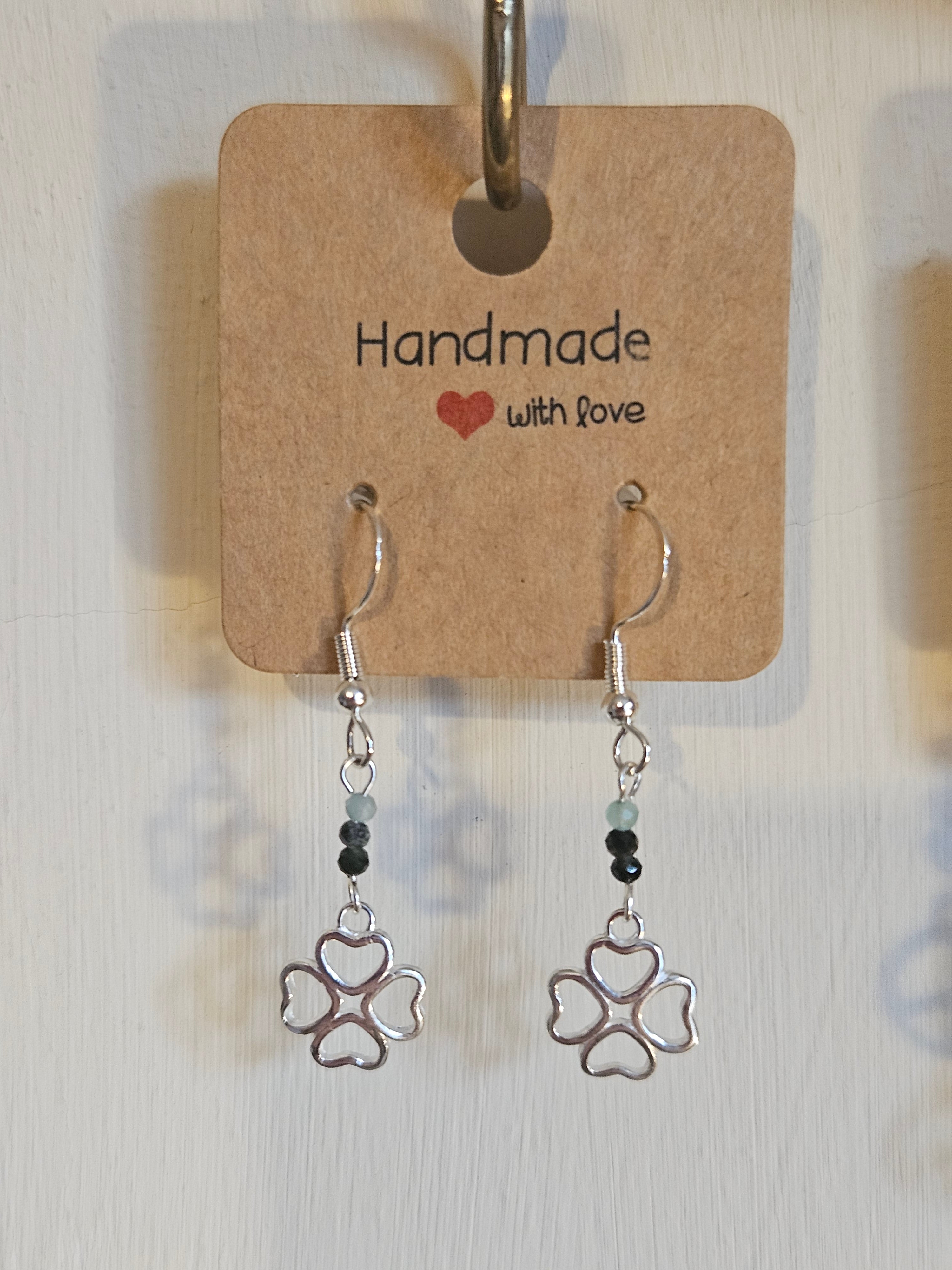 Pair of silver earrings with 4 leaf clover design on a 'Handmade with Love' card.