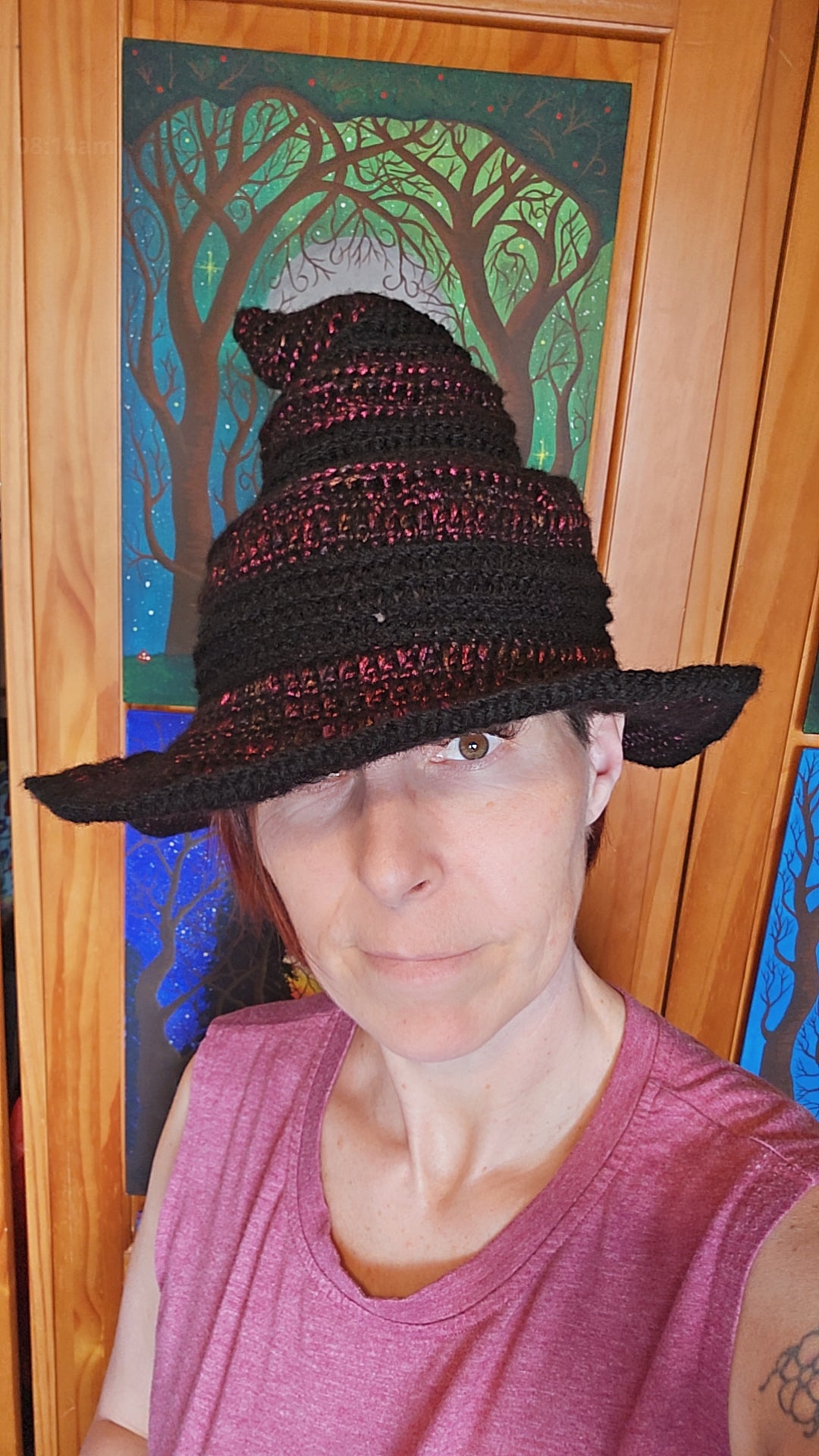 Person wearing a black and red crocheted hat in front of a decorative door with tree designs.