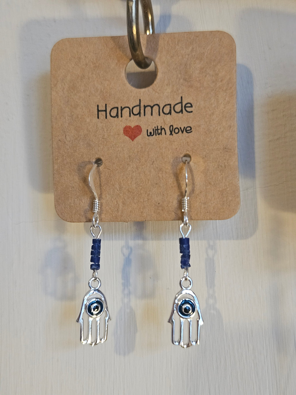 Pair of silver hand-shaped earrings with blue beads on a 'Handmade with Love' card.