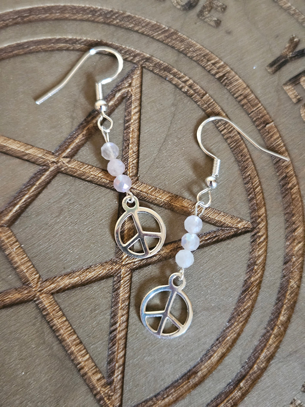 Silver peace symbol earrings with beaded chain on a textured surface