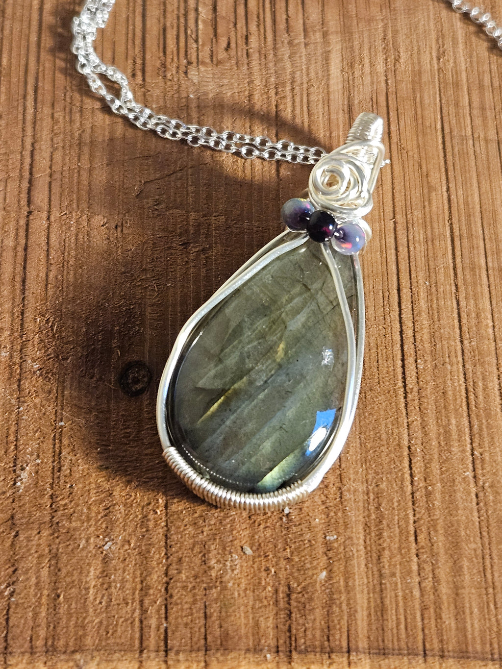 Teardrop-shaped labradorite pendant on a chain against a wooden background
