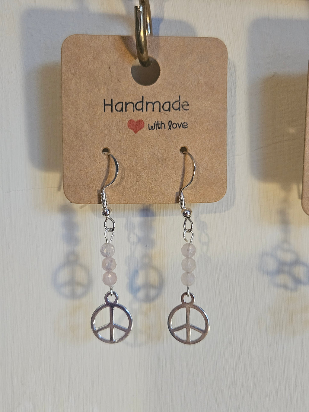 Pair of earrings with peace sign design on a 'Handmade with Love' card.