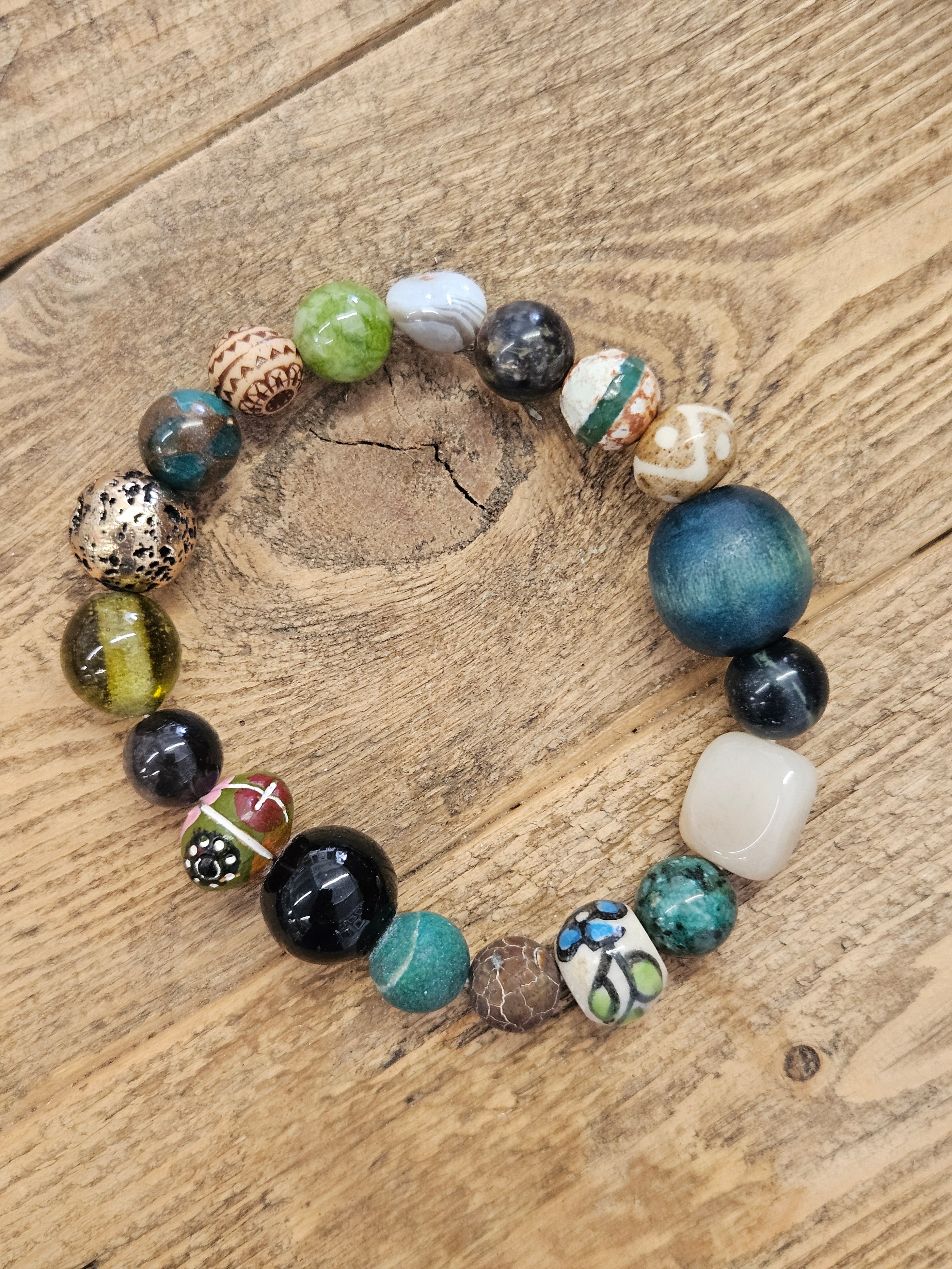 A handmade beaded stretch bracelet made of various colorful, patterned, and textured glass beads, displayed on a rustic wooden surface.