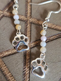 Silver paw print earrings with beaded chain on a wooden surface