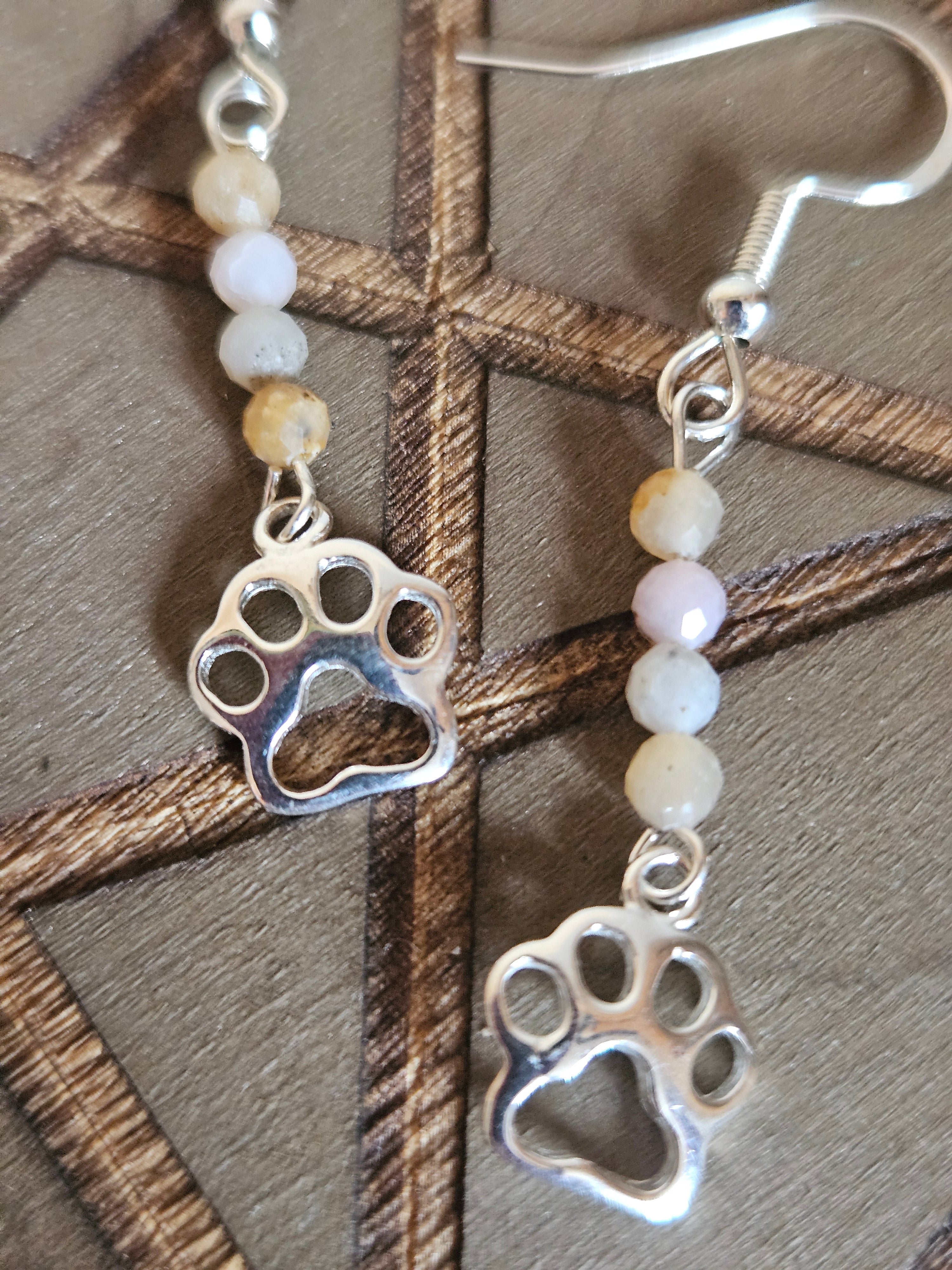 Silver paw print earrings with beaded chain on a wooden surface