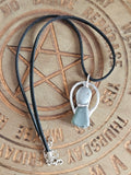 A black cord necklace with a silver-toned pendant featuring two smooth, rounded pale blue-green stones, displayed on a wooden board engraved with a pentagram 