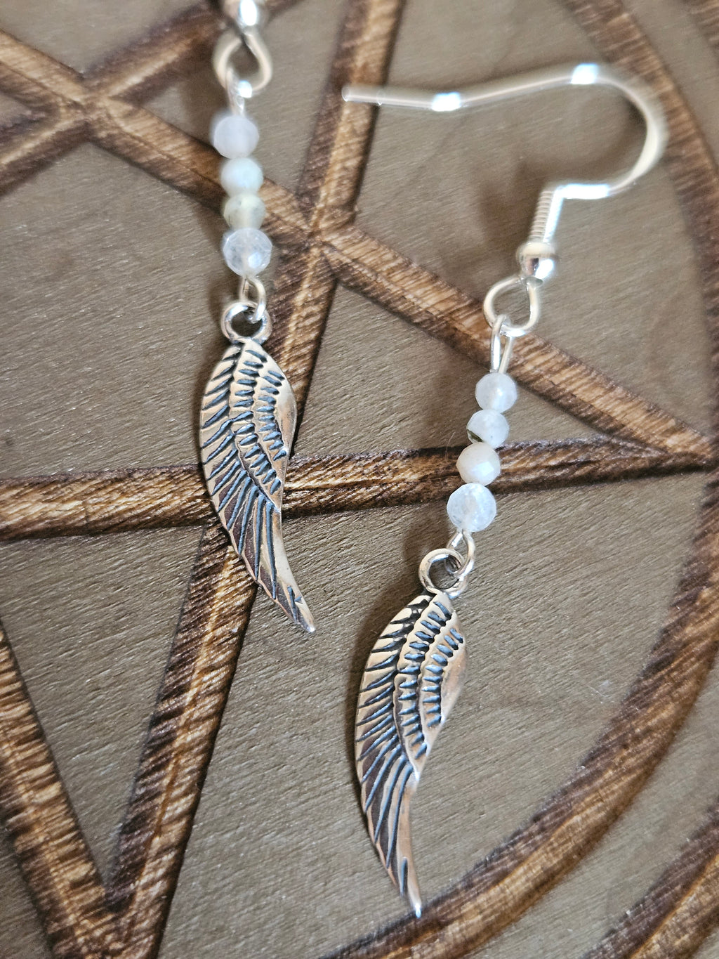 Silver wing-shaped earrings with beaded chain on a wooden surface