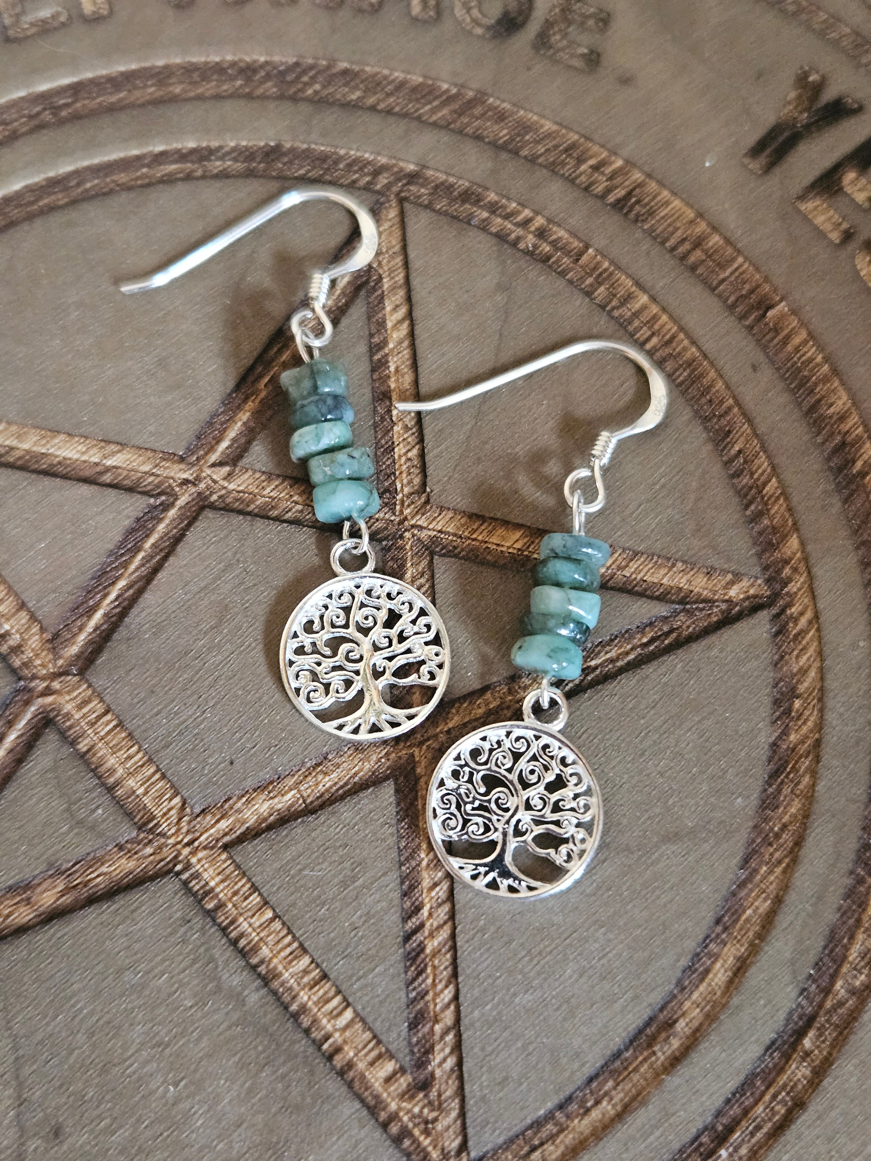 Silver tree of life earrings with green beads on a wooden surface
