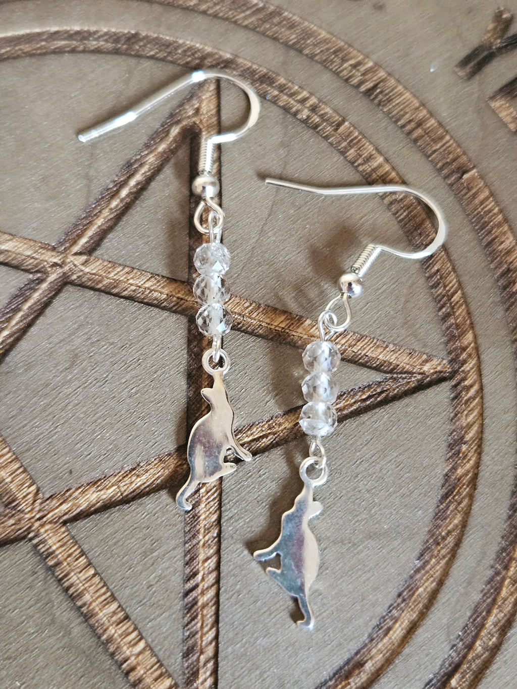 Silver cat-shaped earrings with clear beads on a wooden surface