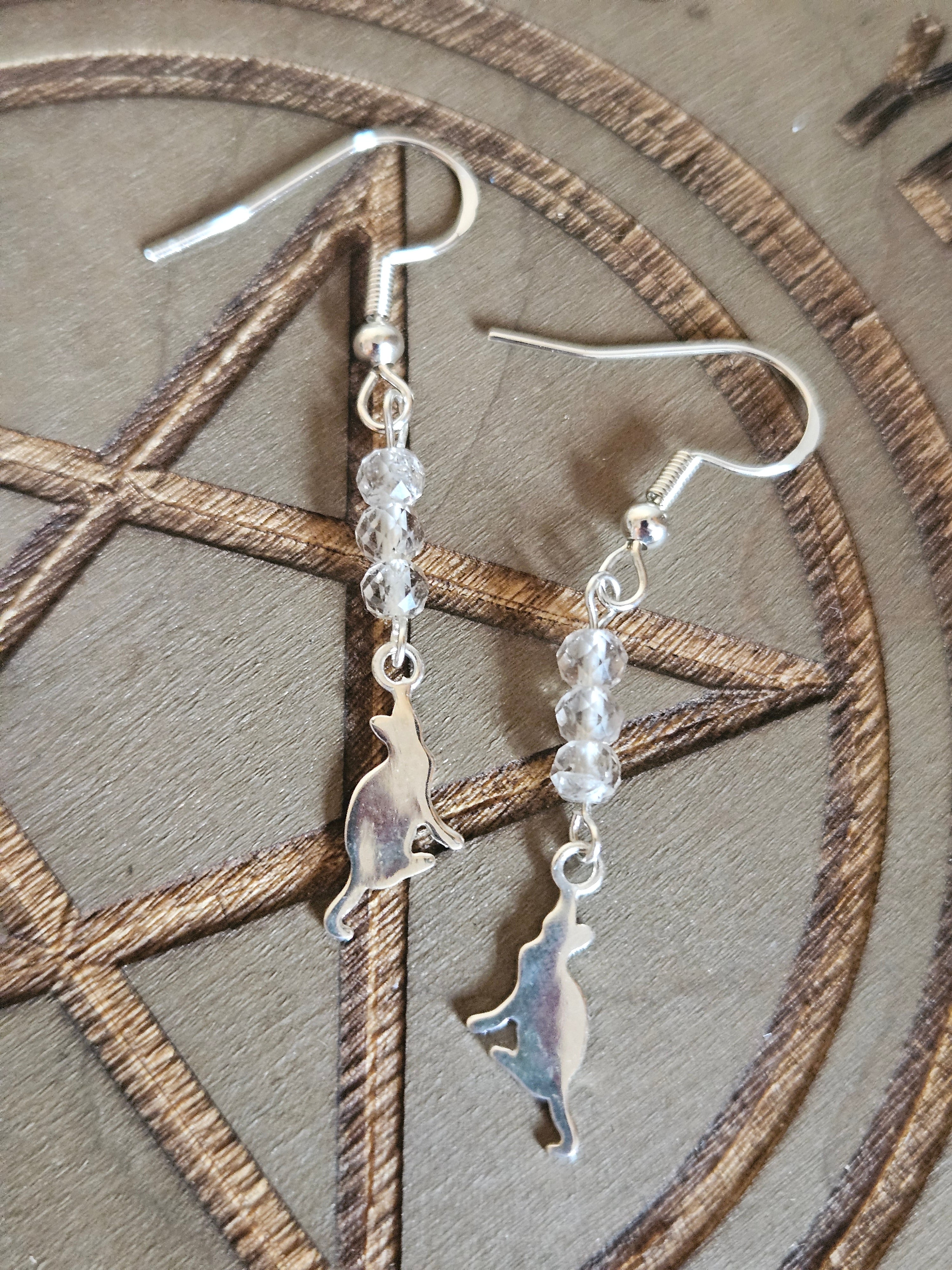 Silver cat-shaped earrings with clear beads on a wooden surface