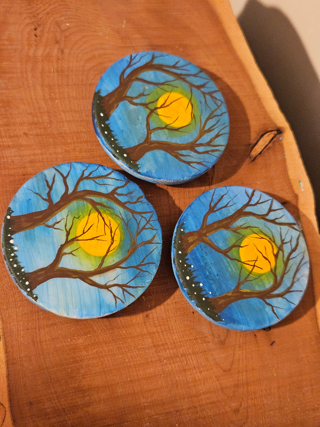Three circular artworks with tree and sun designs on a wooden surface
