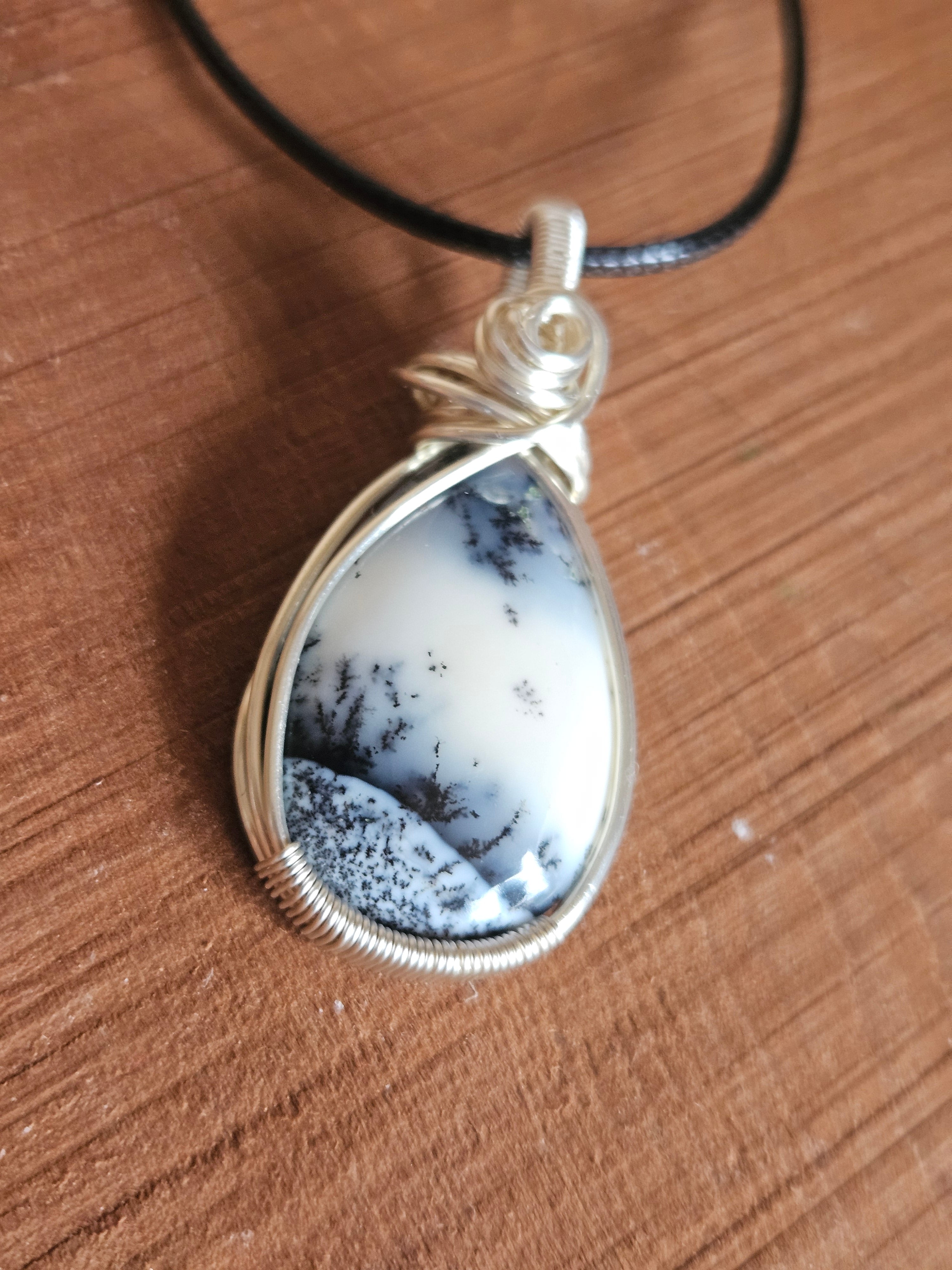 Teardrop-shaped pendant with a speckled stone on a wooden surface