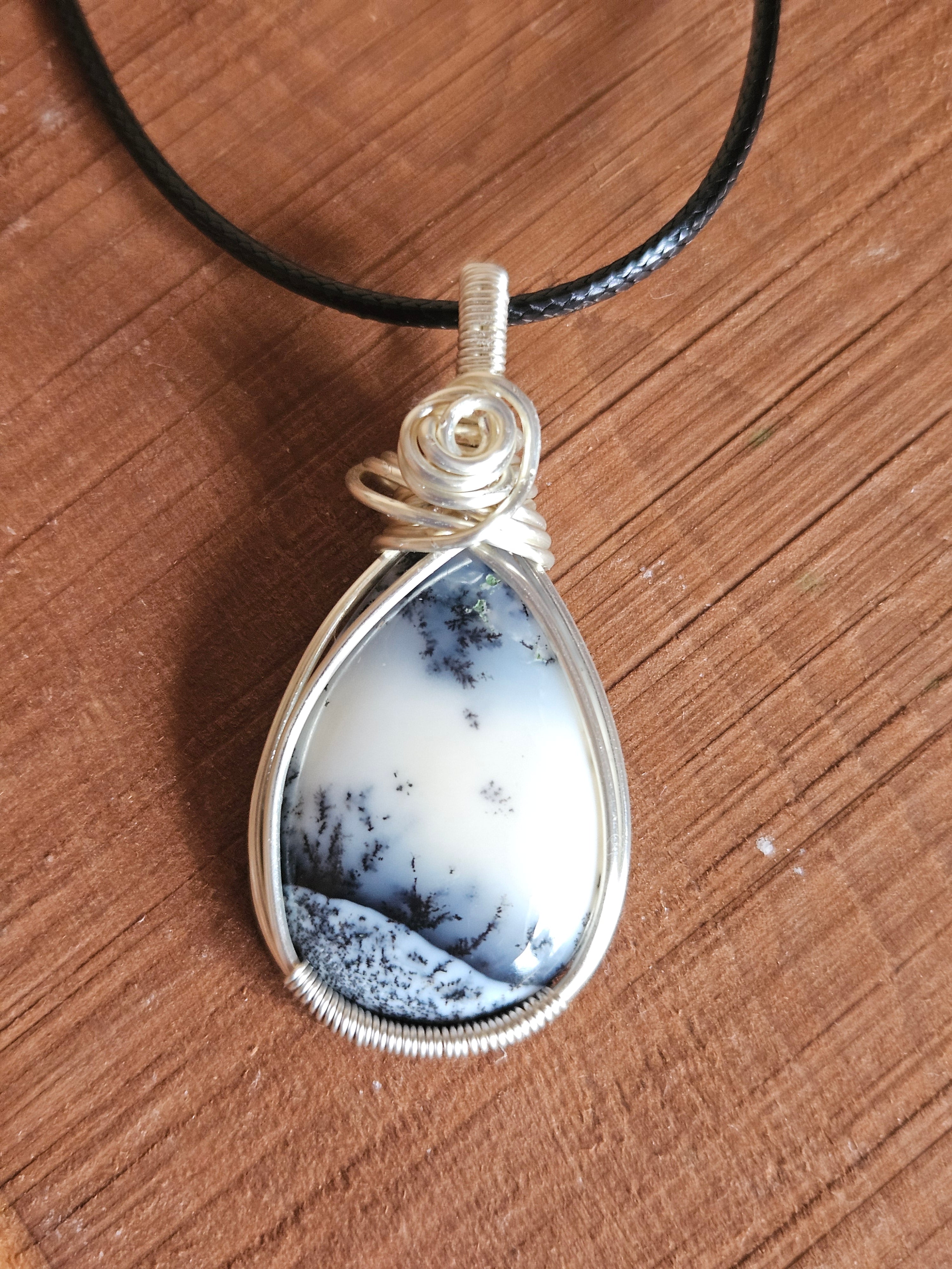 Teardrop-shaped pendant with black and white pattern on a wooden surface