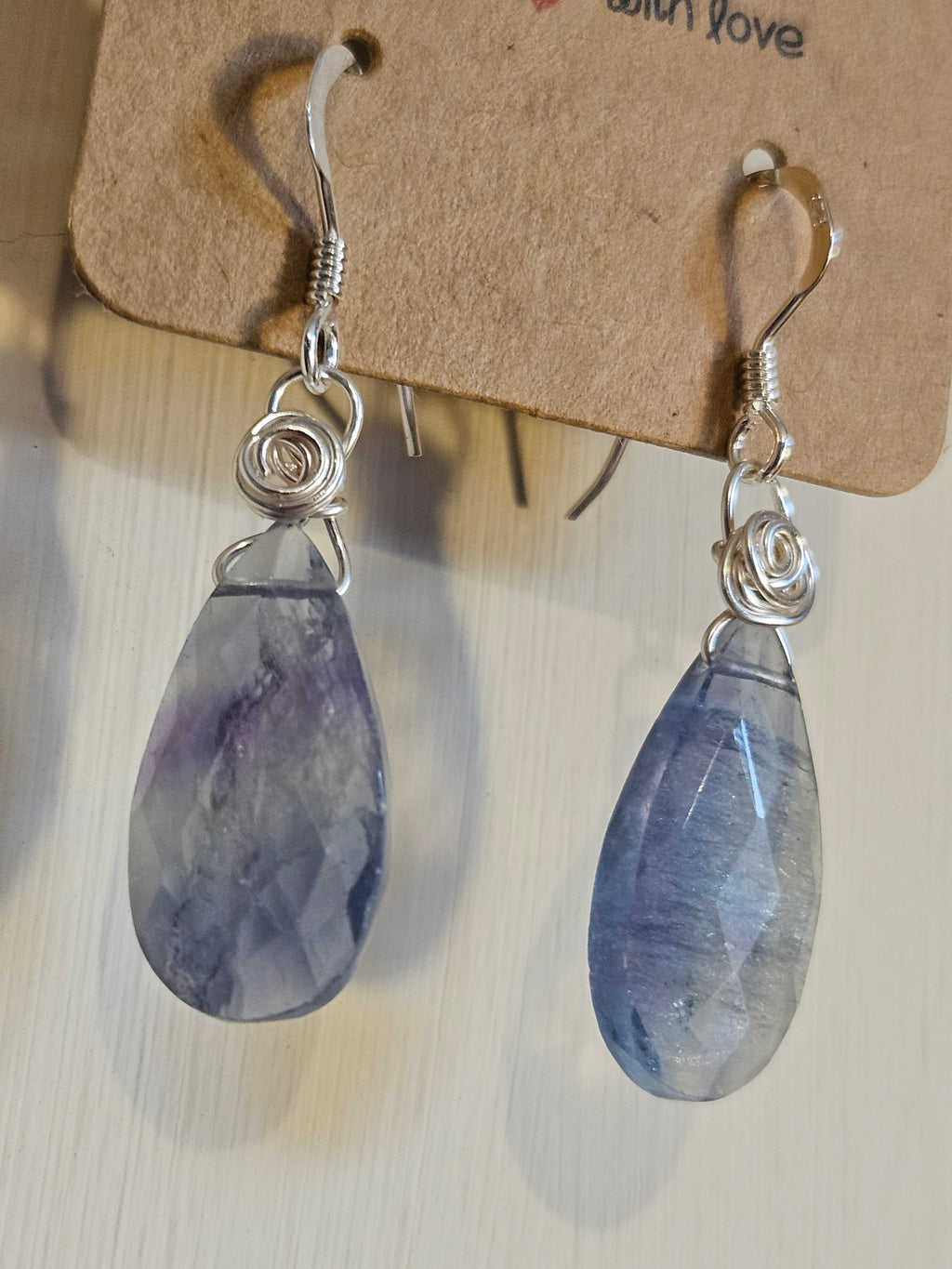 Teardrop-shaped earrings with purple stones on a cardboard backing.