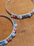 Silver hoop earrings with multicolored beads on a wooden surface