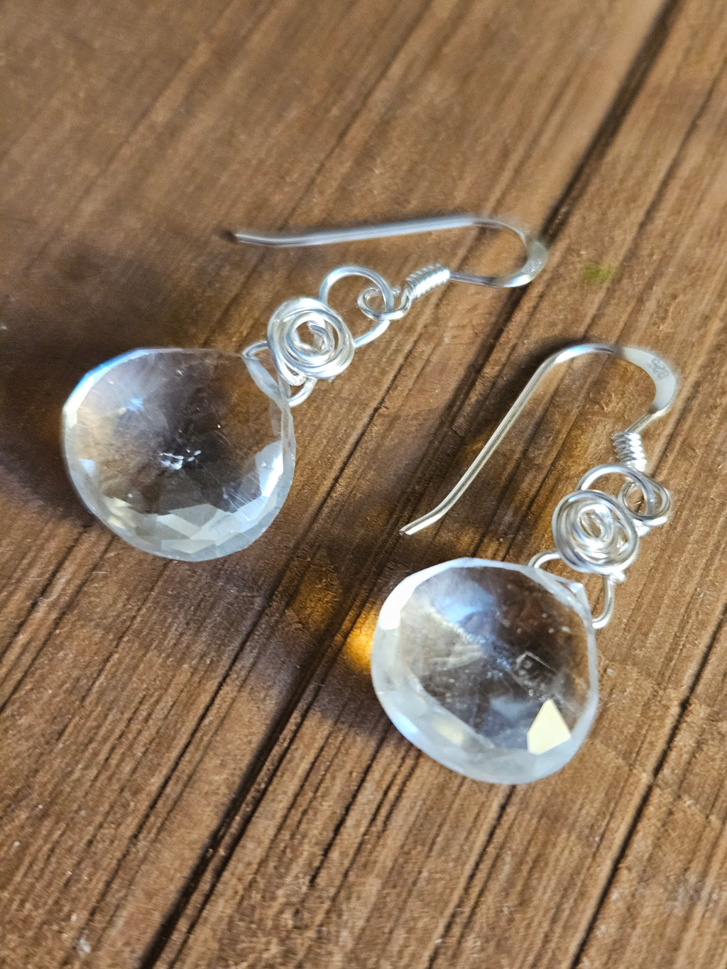 Silver earrings with clear gemstones on a wooden surface