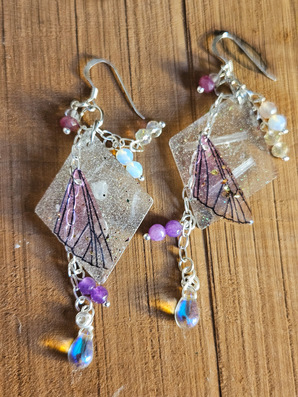 Butterfly-themed earrings with gemstones on a wooden surface