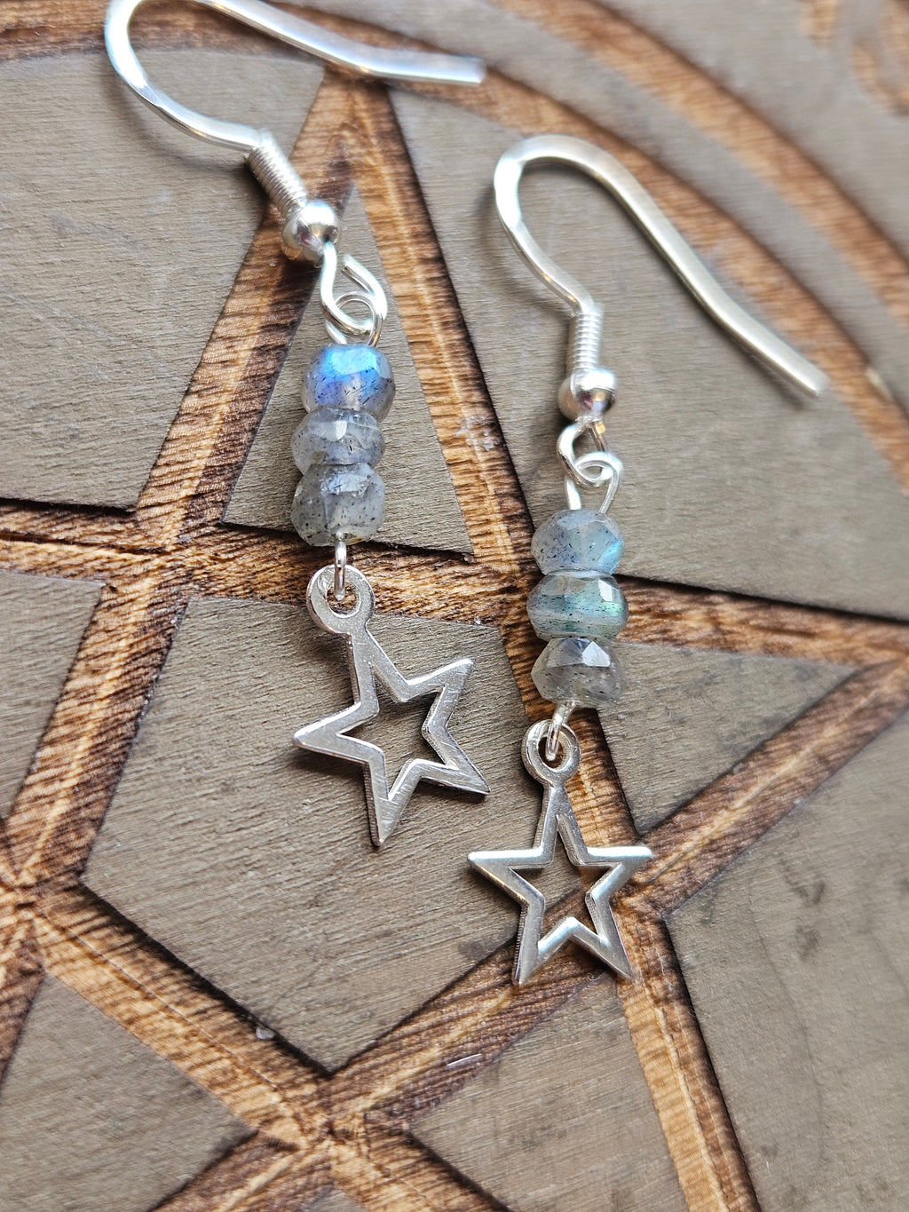 A pair of sterling silver dangle earrings with three faceted gray Labradorite beads and an open star charm, displayed on a wooden background.