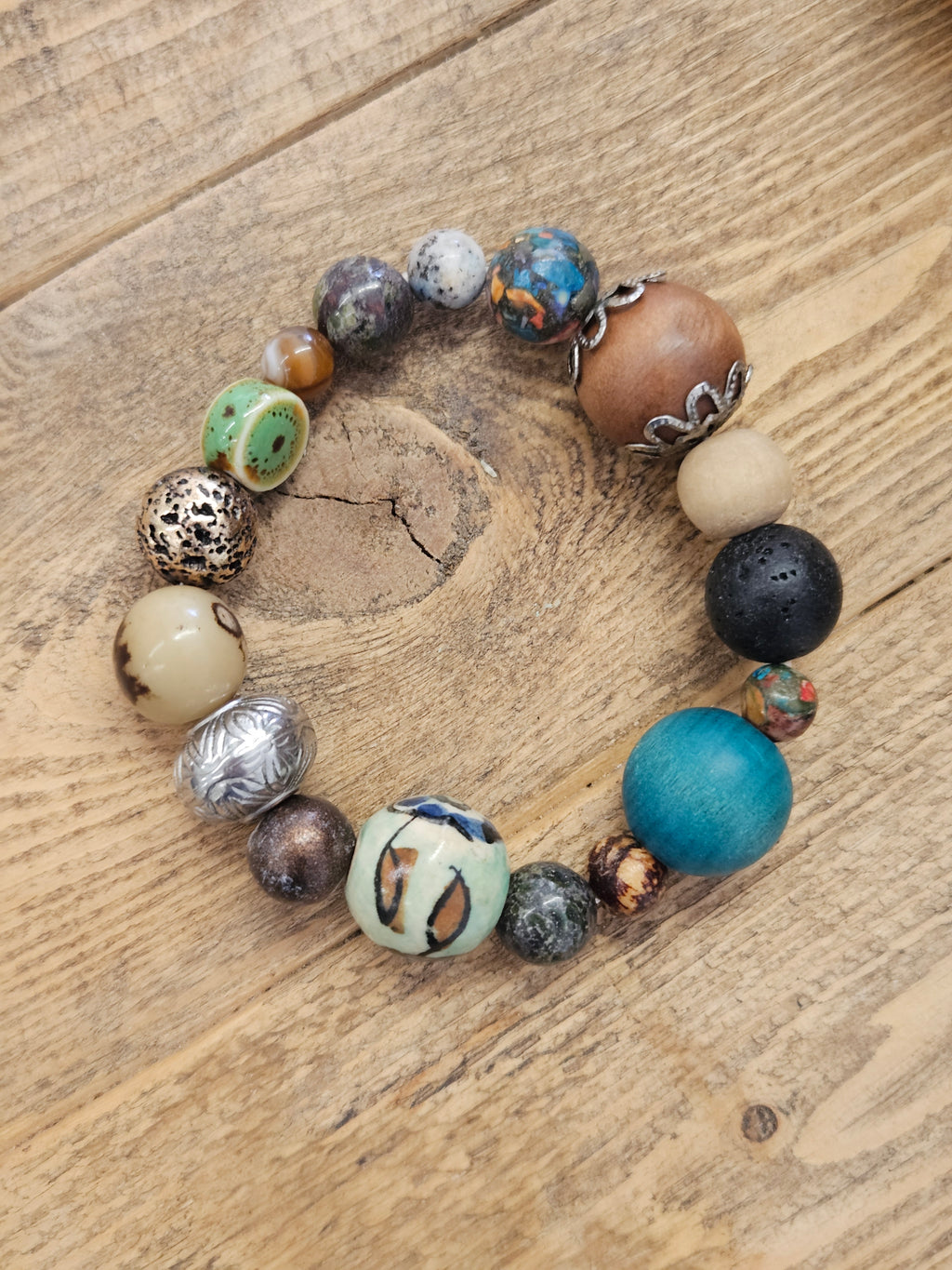 A handmade beaded bracelet with a variety of textured, patterned, and solid beads in multiple colors, displayed on a rustic wooden surface.