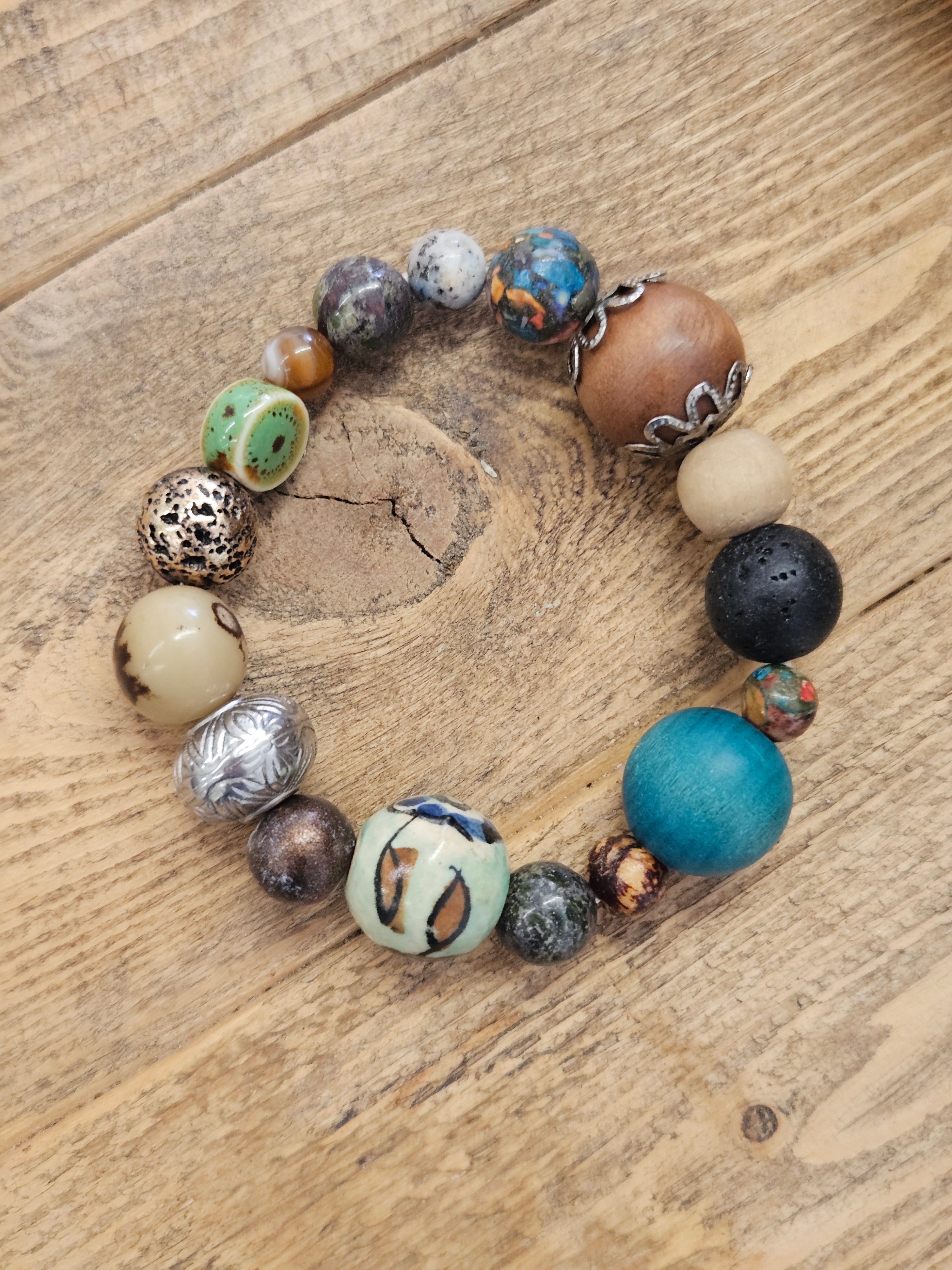 A handmade beaded bracelet with a variety of textured, patterned, and solid beads in multiple colors, displayed on a rustic wooden surface.