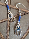 Silver earrings with hand designs and blue beads on a wooden surface