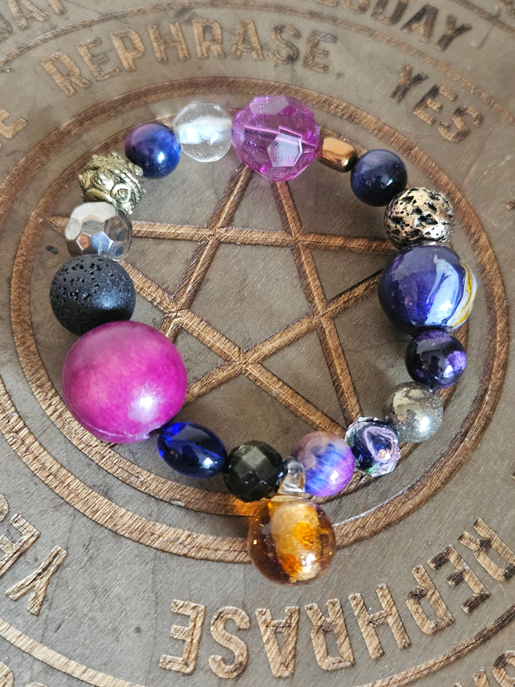 A beaded stretch boho bracelet with a variety of colorful, textured, and patterned beads arranged in a circle on a wooden pentagram background.