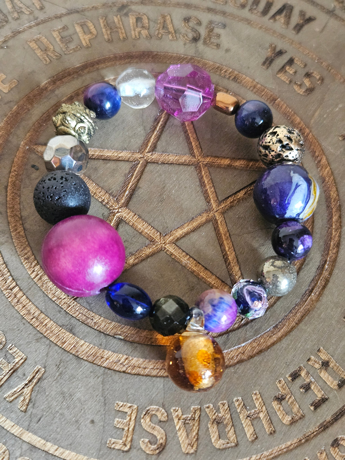 A beaded stretch boho bracelet with a variety of colorful, textured, and patterned beads arranged in a circle on a wooden pentagram background.