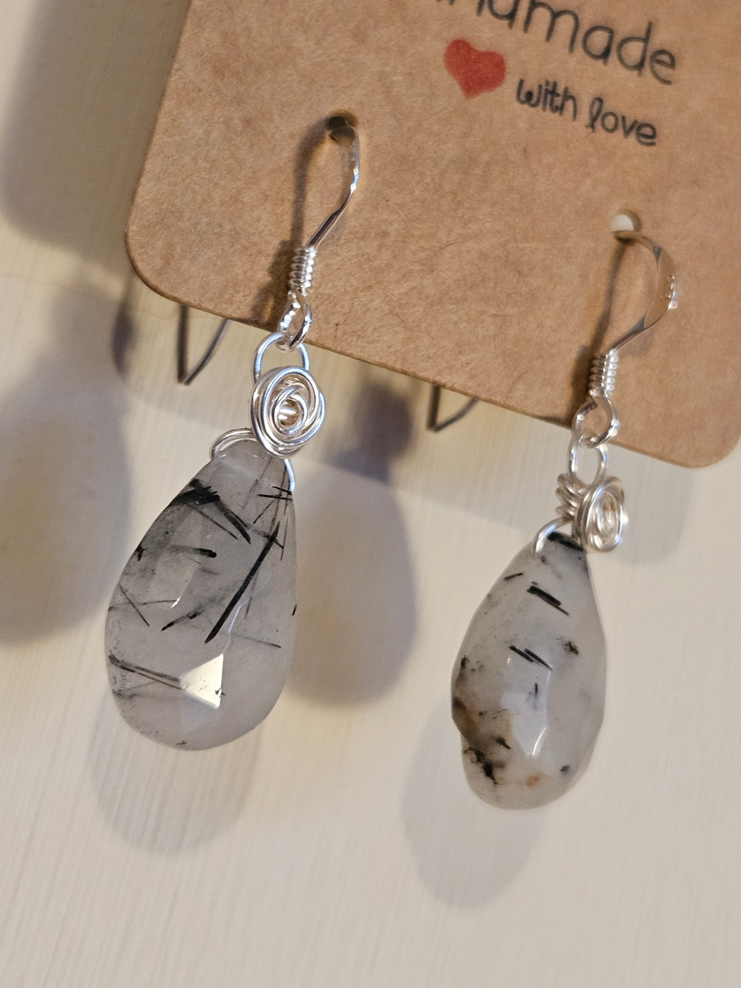 Earrings with Tourmaline in Quarts pendants on a beige background