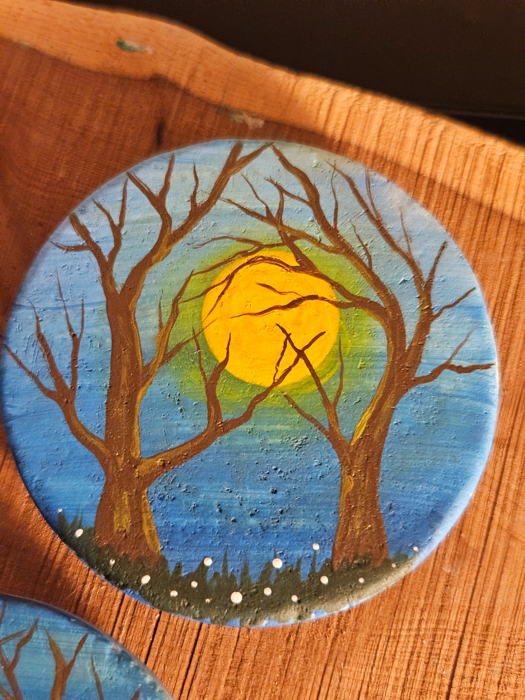 Round painted magnet with a tree and sun design on a wooden surface