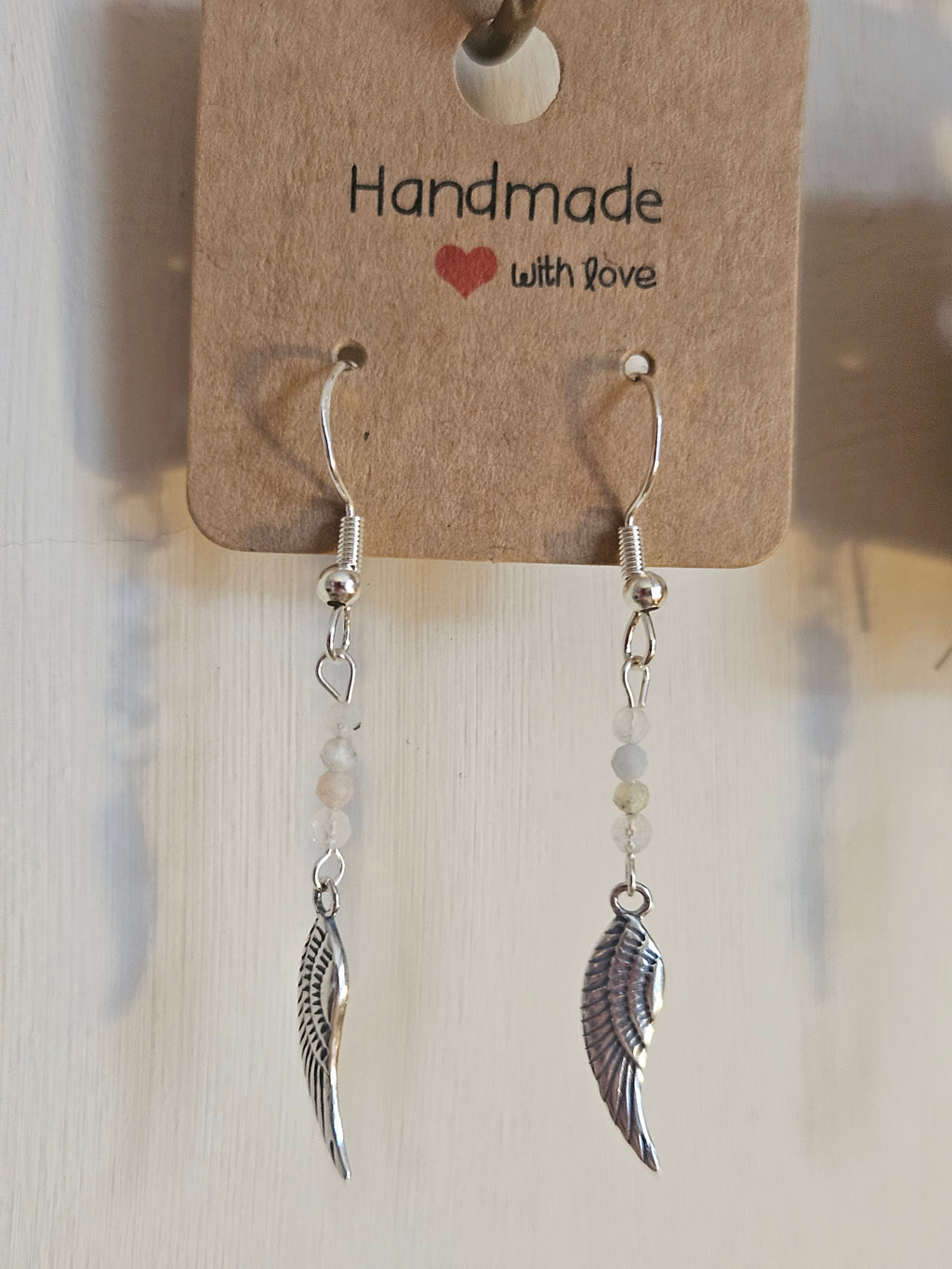 Silver wing-shaped earrings on a 'Handmade with Love' card.