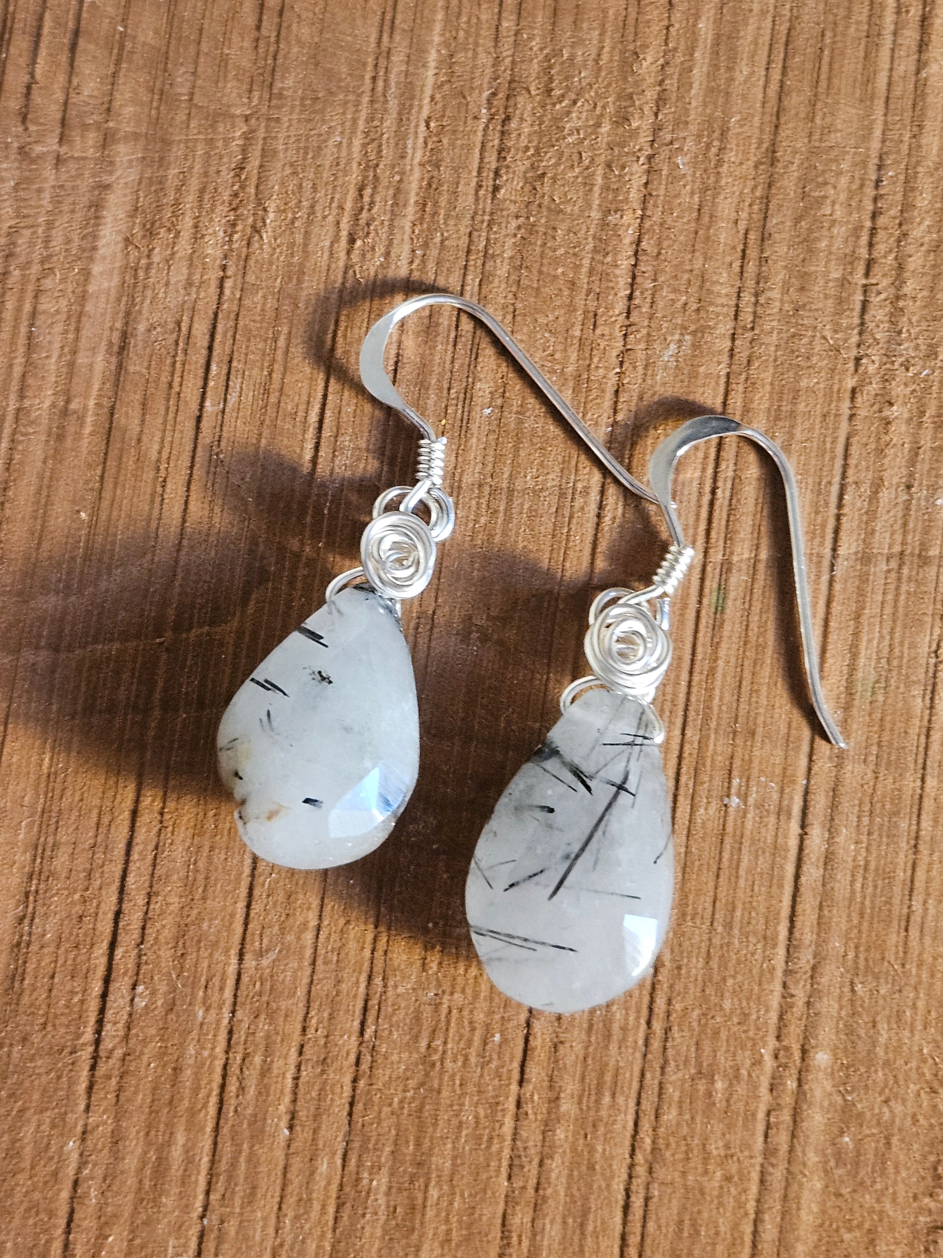 Pair of earrings with teardrop-shaped gemstones on a wooden surface