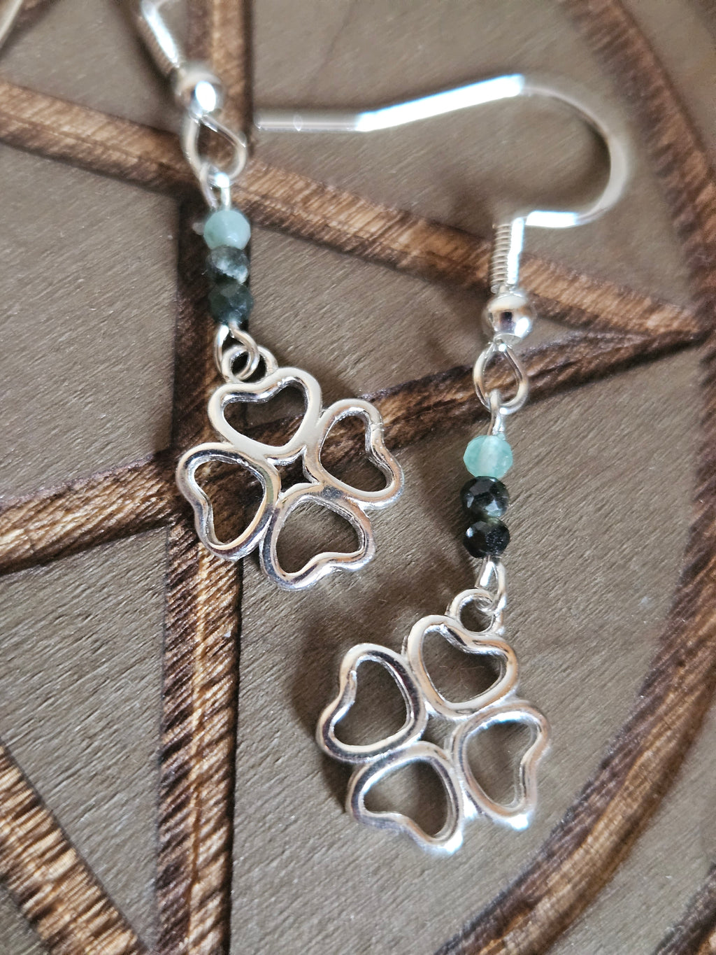Silver four-leaf clover earrings with green beads on a wooden surface