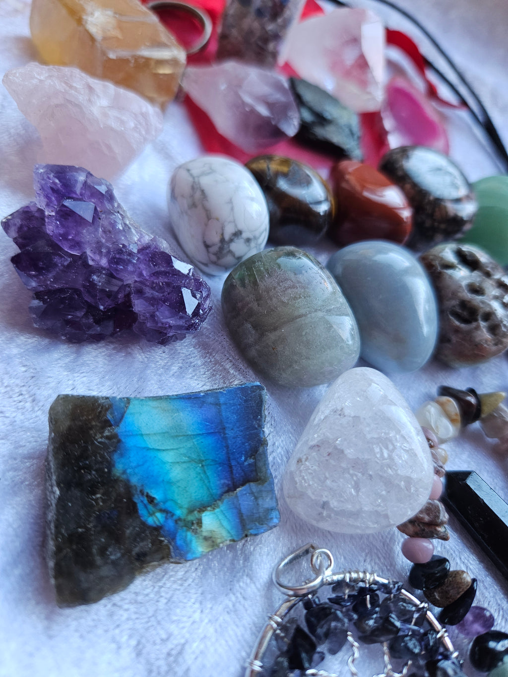 A collection of raw and polished crystals, gemstones, and a labradorite pendant displayed on a white textured fabric background.