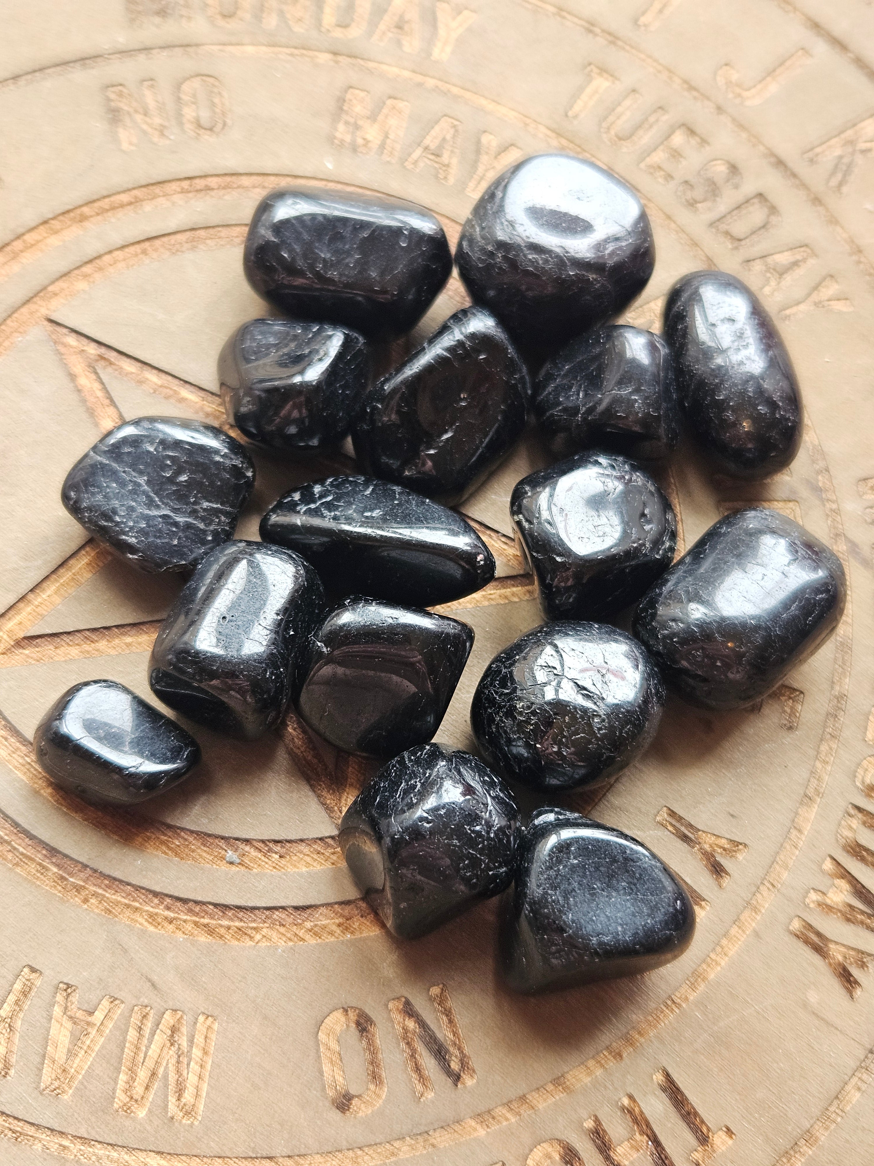 A pile of polished black tumbled stones, Black Tourmaline, arranged on a wood coaster with engraved text and a star design