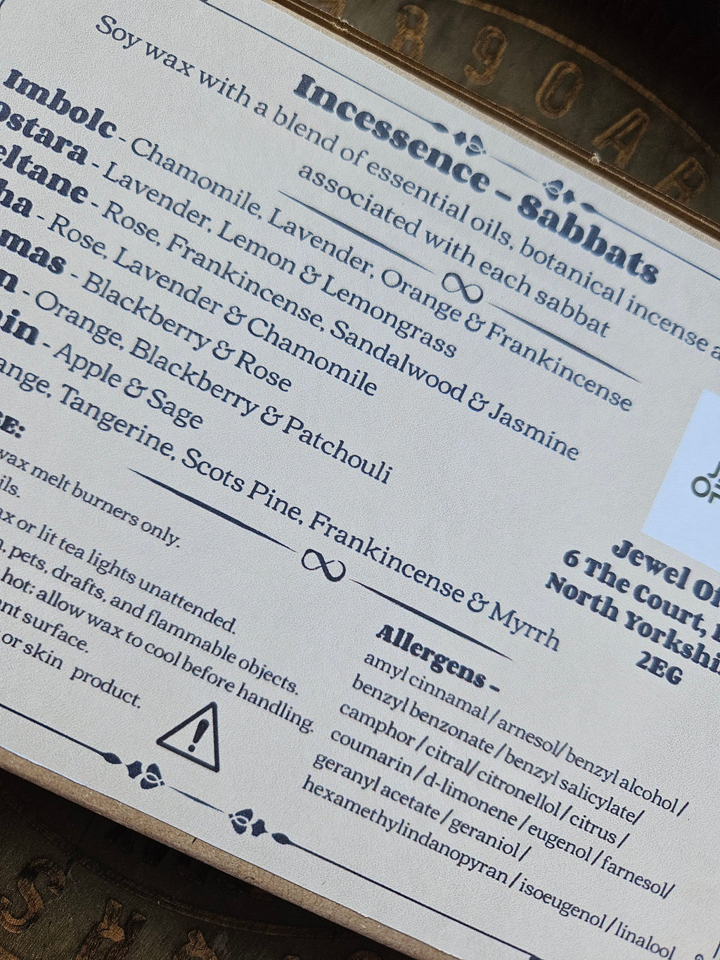 A close-up of a printed product CLP label showing scent names and ingredient lists, photographed on a textured surface.