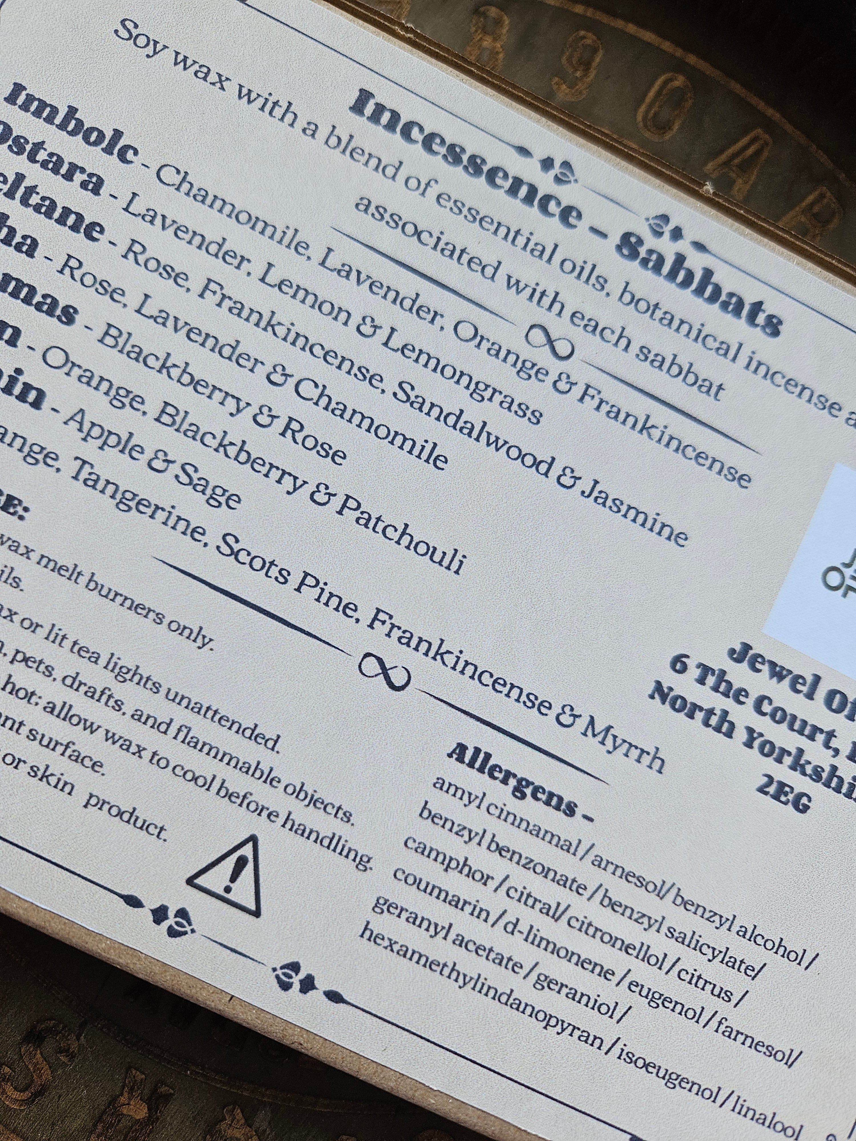 A close-up of a printed product CLP label showing scent names and ingredient lists, photographed on a textured surface.
